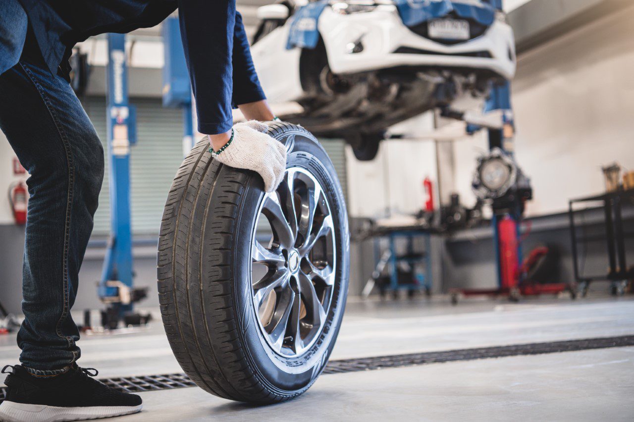Male mechanic hold and rolling tire at repairing service garage background. Technician man replacing winter and summer tyre for safety road trip. Transportation and automotive maintenance concept Male mechanic hold and rolling tire at repairing service garage background. Technician man replacing winter and summer tyre for safety road trip. Transportation and automotive maintenance concept